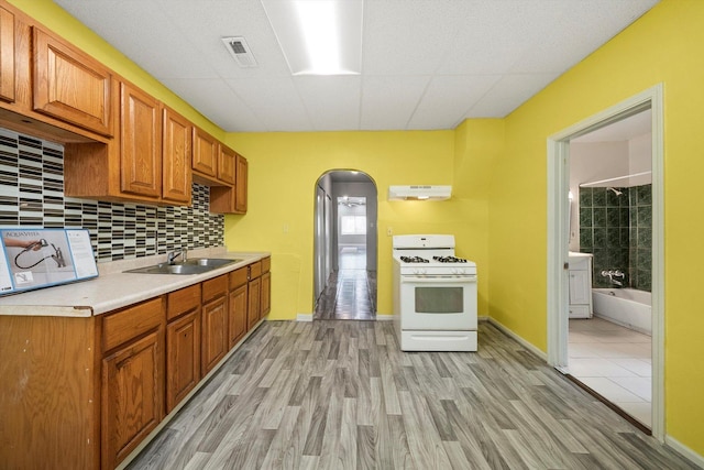 kitchen featuring white gas range oven, a sink, light countertops, arched walkways, and under cabinet range hood