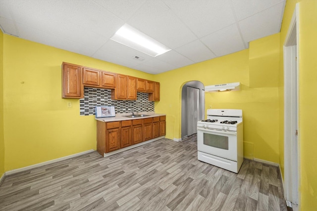 kitchen with white gas range, a paneled ceiling, under cabinet range hood, a sink, and light wood finished floors