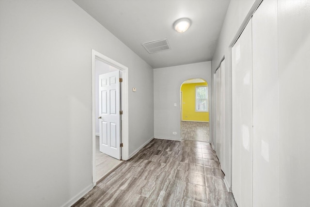 hallway with arched walkways, baseboards, wood finished floors, and visible vents