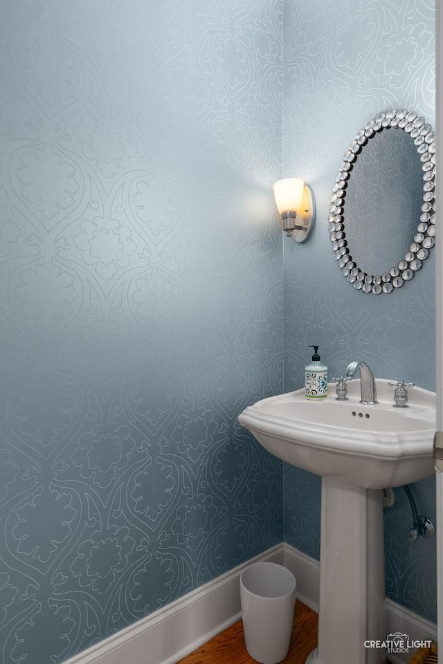 bathroom featuring wallpapered walls, a sink, baseboards, and wood finished floors