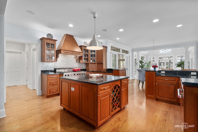 kitchen featuring a kitchen island, dark countertops, stove, custom range hood, and light wood-style flooring