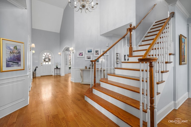 entrance foyer with an inviting chandelier, stairs, wood finished floors, a high ceiling, and arched walkways
