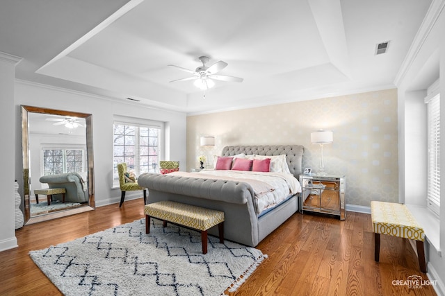 bedroom with visible vents, crown molding, wood finished floors, a raised ceiling, and baseboards