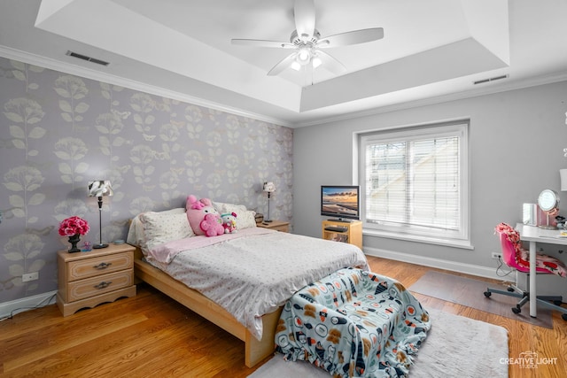 bedroom with visible vents, crown molding, wood finished floors, a raised ceiling, and baseboards