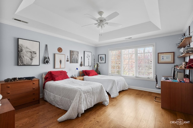 bedroom with visible vents, crown molding, light wood-type flooring, baseboards, and a tray ceiling