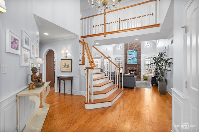 staircase with a high ceiling, a brick fireplace, arched walkways, wood finished floors, and ornamental molding