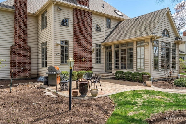 back of house with a shingled roof, a patio area, a fire pit, and a chimney