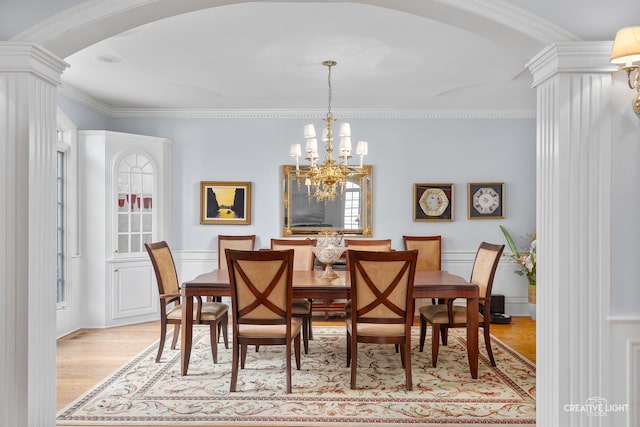 dining space featuring arched walkways, light wood-style flooring, a notable chandelier, and ornamental molding