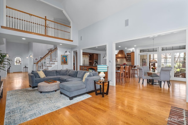 living room with visible vents, light wood-style flooring, stairway, and a towering ceiling