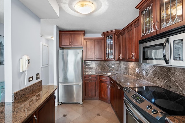 kitchen featuring decorative backsplash, appliances with stainless steel finishes, a sink, dark stone countertops, and glass insert cabinets