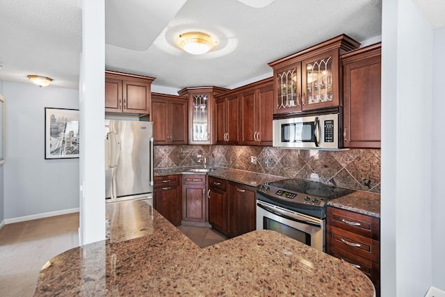 kitchen with baseboards, appliances with stainless steel finishes, dark stone countertops, and tasteful backsplash
