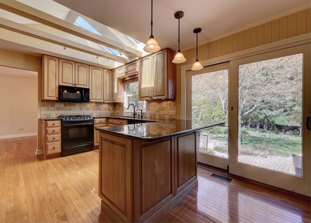 kitchen featuring backsplash, a skylight, light wood finished floors, and black appliances