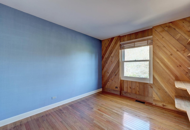 unfurnished room with baseboards, wood walls, wood finished floors, and visible vents