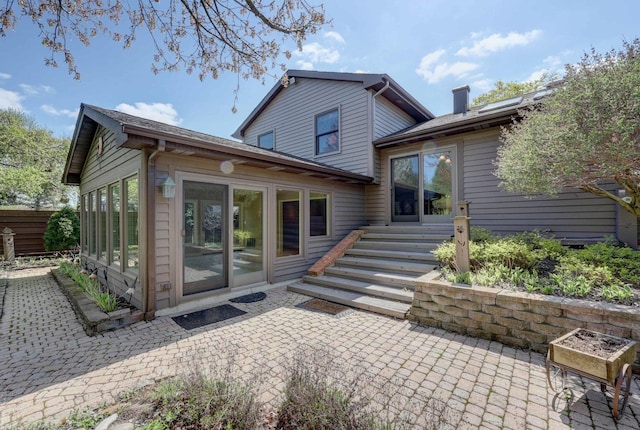 rear view of house featuring a sunroom, a chimney, and a patio area