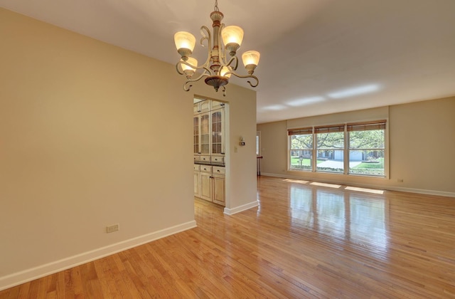 unfurnished room featuring baseboards, light wood finished floors, and a notable chandelier