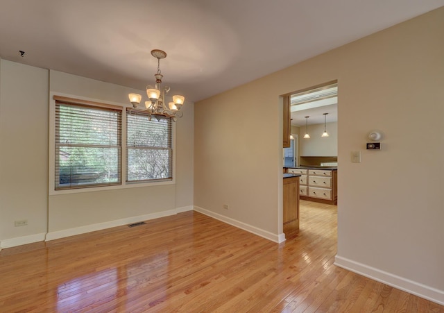 unfurnished room with baseboards, a notable chandelier, visible vents, and light wood-style floors
