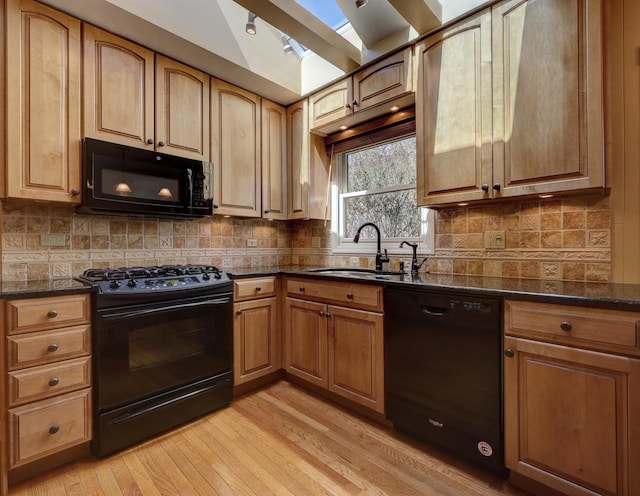 kitchen with light wood-type flooring, tasteful backsplash, a sink, dark stone countertops, and black appliances