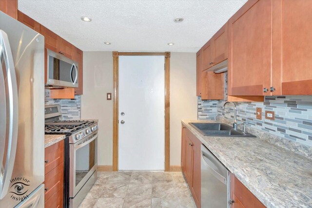 kitchen with stainless steel appliances, a sink, a textured ceiling, brown cabinetry, and backsplash