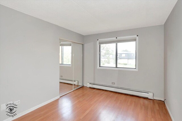 empty room with baseboard heating, light wood finished floors, and baseboards
