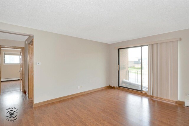 empty room featuring wood finished floors, a baseboard heating unit, a textured ceiling, and baseboards