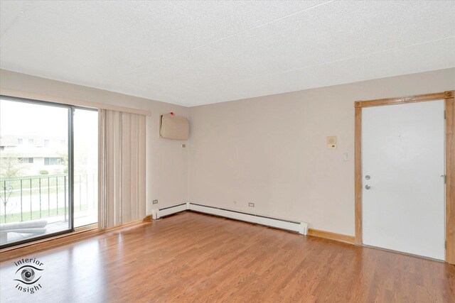 spare room featuring wood finished floors, healthy amount of natural light, baseboard heating, a baseboard radiator, and a textured ceiling
