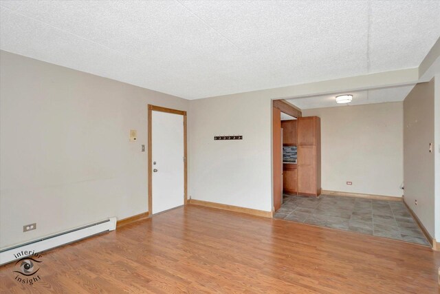 empty room with wood finished floors, plenty of natural light, a baseboard heating unit, and a textured ceiling