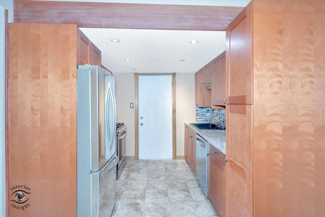 kitchen with stainless steel appliances, a sink, light countertops, brown cabinets, and backsplash