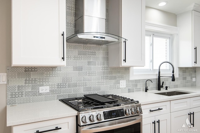kitchen featuring gas range, a sink, light countertops, white cabinets, and wall chimney exhaust hood