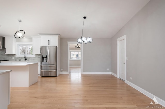 kitchen with stainless steel fridge with ice dispenser, light countertops, tasteful backsplash, a sink, and light wood-style flooring