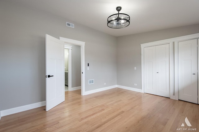 unfurnished bedroom featuring visible vents, light wood-style floors, baseboards, and two closets