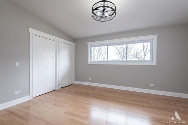 unfurnished bedroom with baseboards, multiple closets, lofted ceiling, and light wood-style floors
