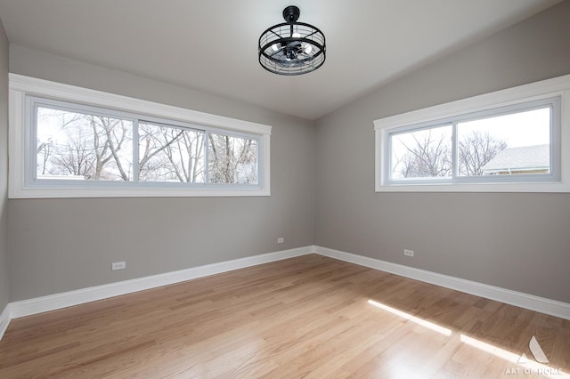 spare room with light wood-type flooring, baseboards, and vaulted ceiling