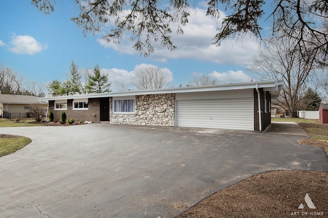 ranch-style home featuring an attached garage, aphalt driveway, and stone siding