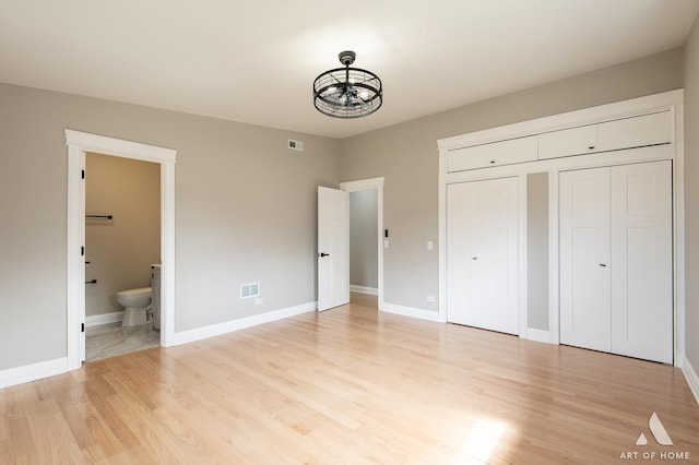 unfurnished bedroom featuring baseboards, visible vents, ensuite bathroom, and light wood-type flooring