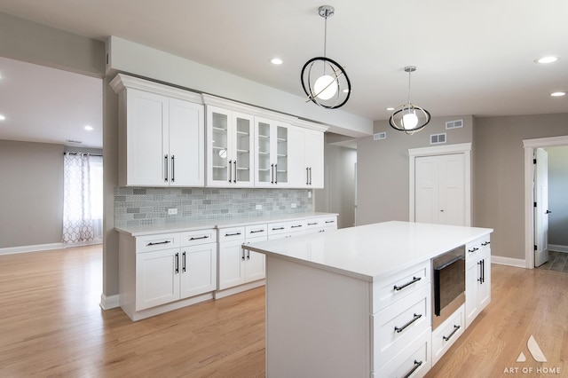 kitchen featuring backsplash, visible vents, built in microwave, baseboards, and light wood finished floors