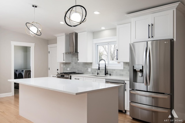 kitchen featuring decorative backsplash, washing machine and dryer, wall chimney range hood, a sink, and stainless steel appliances