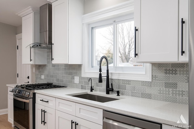 kitchen with wall chimney range hood, white cabinets, a sink, stainless steel appliances, and tasteful backsplash