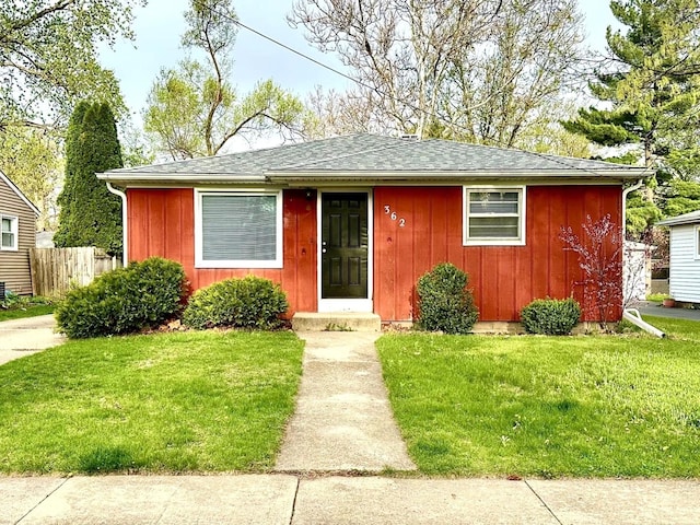 bungalow-style home featuring roof with shingles, fence, board and batten siding, and a front lawn