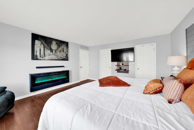 bedroom with visible vents, baseboards, wood finished floors, and a fireplace