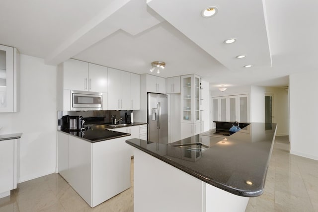 kitchen with dark countertops, a sink, glass insert cabinets, stainless steel appliances, and white cabinetry