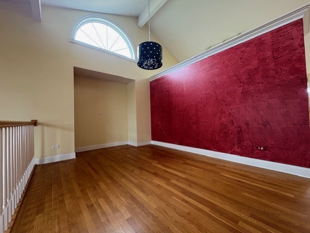 spare room featuring baseboards, beamed ceiling, and wood finished floors