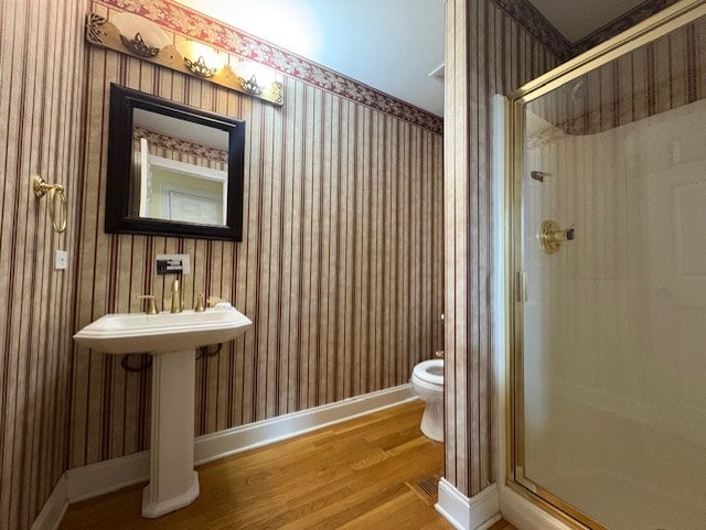 full bathroom with wood finished floors, a stall shower, toilet, and wallpapered walls