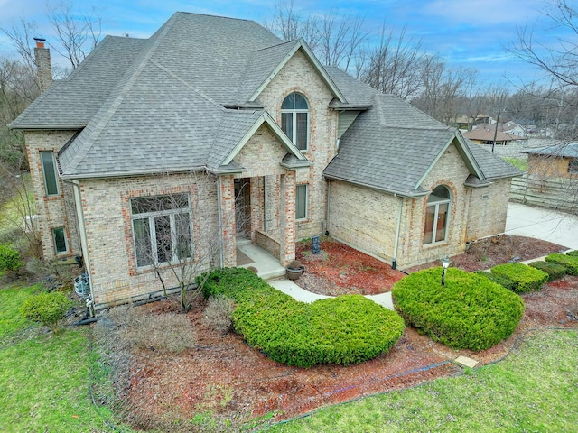 french country inspired facade with brick siding, a shingled roof, and a chimney