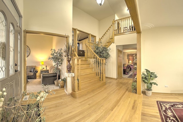 entryway with stairway, wood finished floors, and a towering ceiling