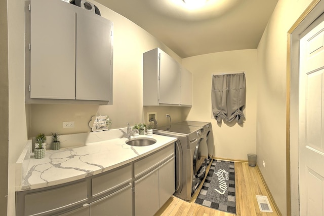 laundry area featuring visible vents, light wood-style floors, washer and clothes dryer, a sink, and cabinet space