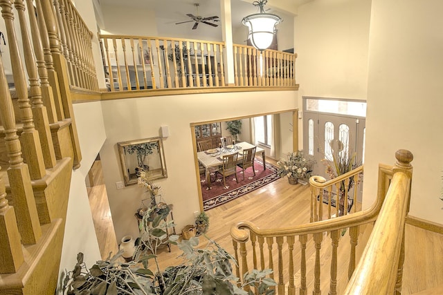 stairway with a ceiling fan, a towering ceiling, and wood finished floors