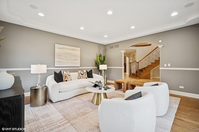 living area featuring visible vents, stairs, wood finished floors, baseboards, and arched walkways