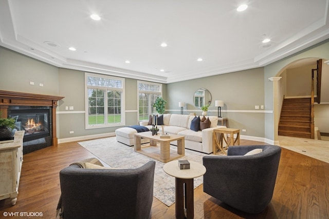 living area with arched walkways, a glass covered fireplace, stairs, baseboards, and wood finished floors