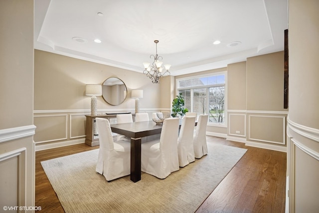 dining space featuring an inviting chandelier, a decorative wall, a tray ceiling, and dark wood finished floors