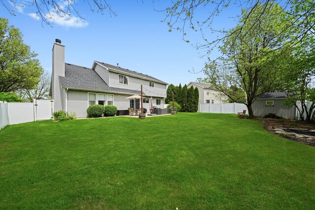 rear view of house with a fenced backyard, a chimney, a yard, and a patio area